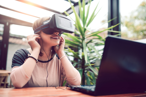 un estudiante se sienta en un escritorio frente a una computadora portátil y mira a través de un auricular VR