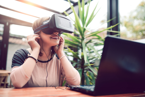 a student sits at a desk in front of a laptop and looks through a VR headset