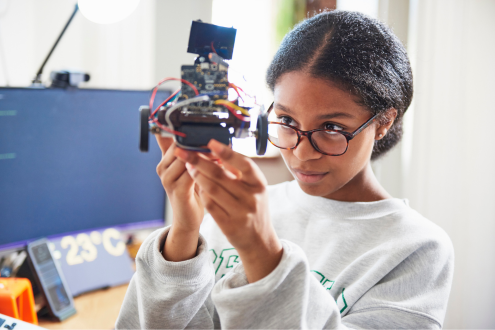 A student studies a robot she's building in a classroom