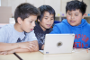 Three elementary school boys huddled around a laptop